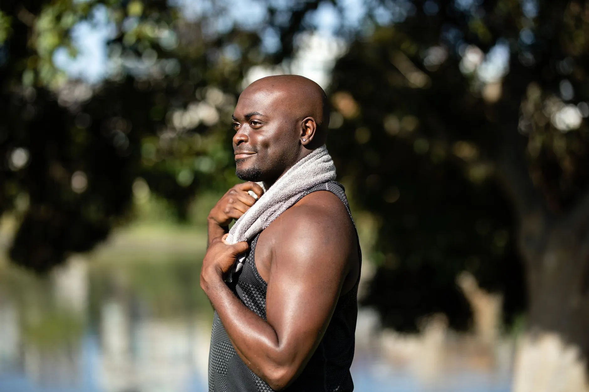 A fit, smiling man with a towel over his shoulder after an outdoor workout