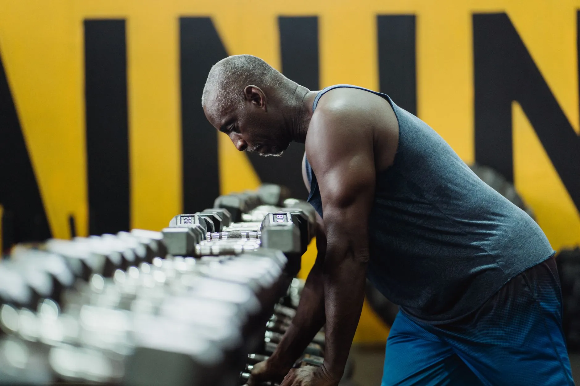 A man in his fifties choosing dumbbells at a gym rack