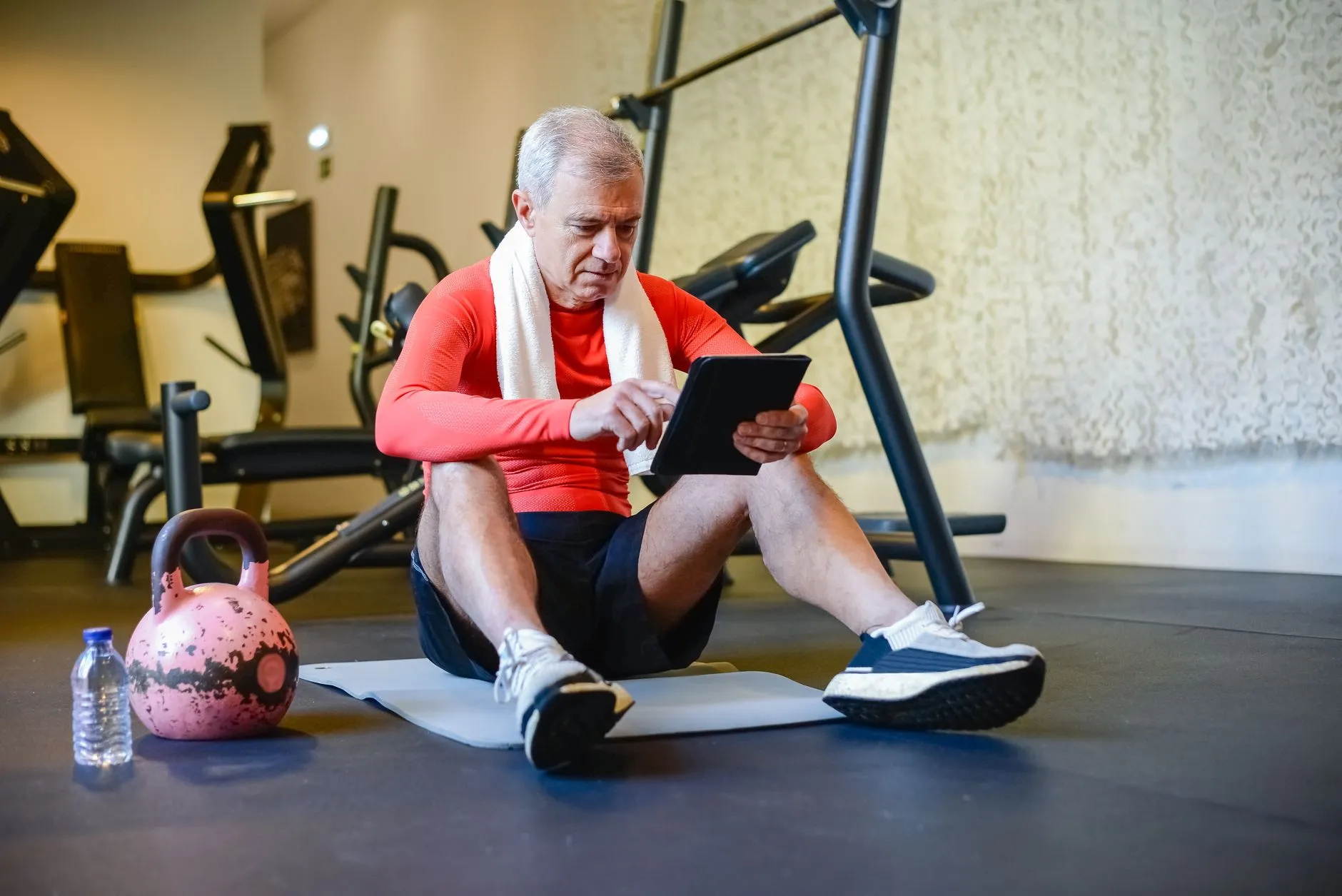 A silver-haired man checking his program on a tablet between sets